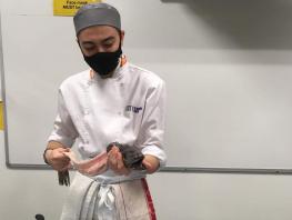 Photo of Robbie McDougall filleting a fish in the college kitchens 