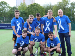 Eight students wearing football strips holding a cup  