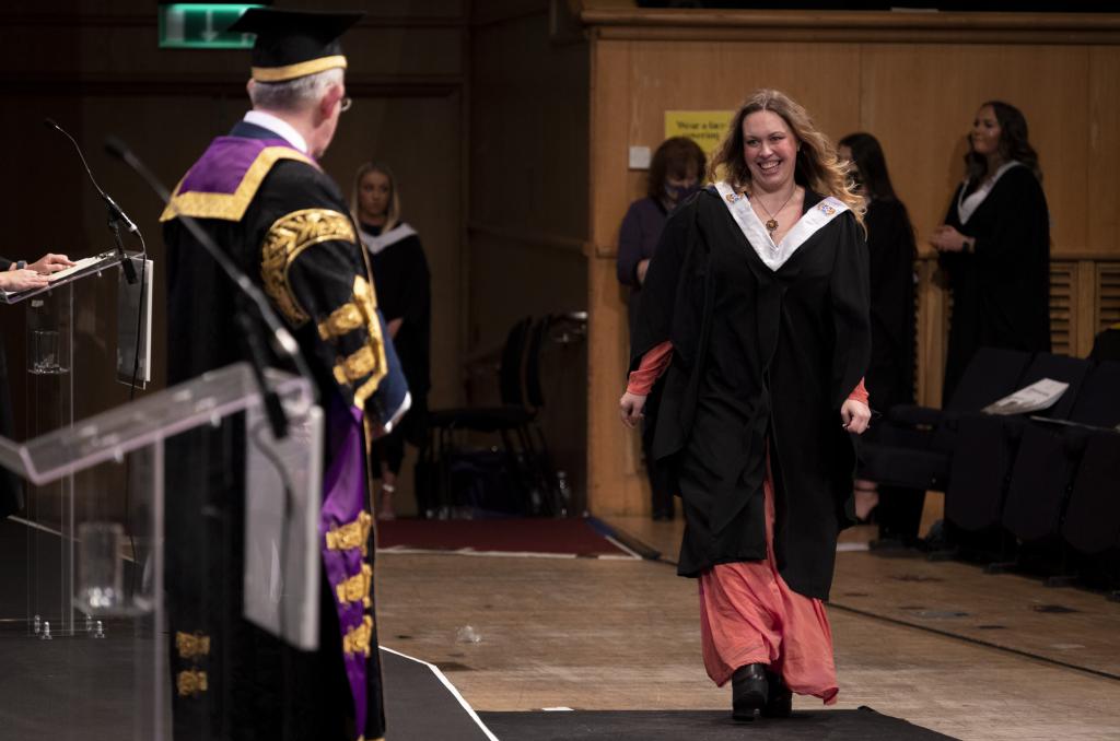 A student in academic robes walking across the stage during the graduation ceremony.