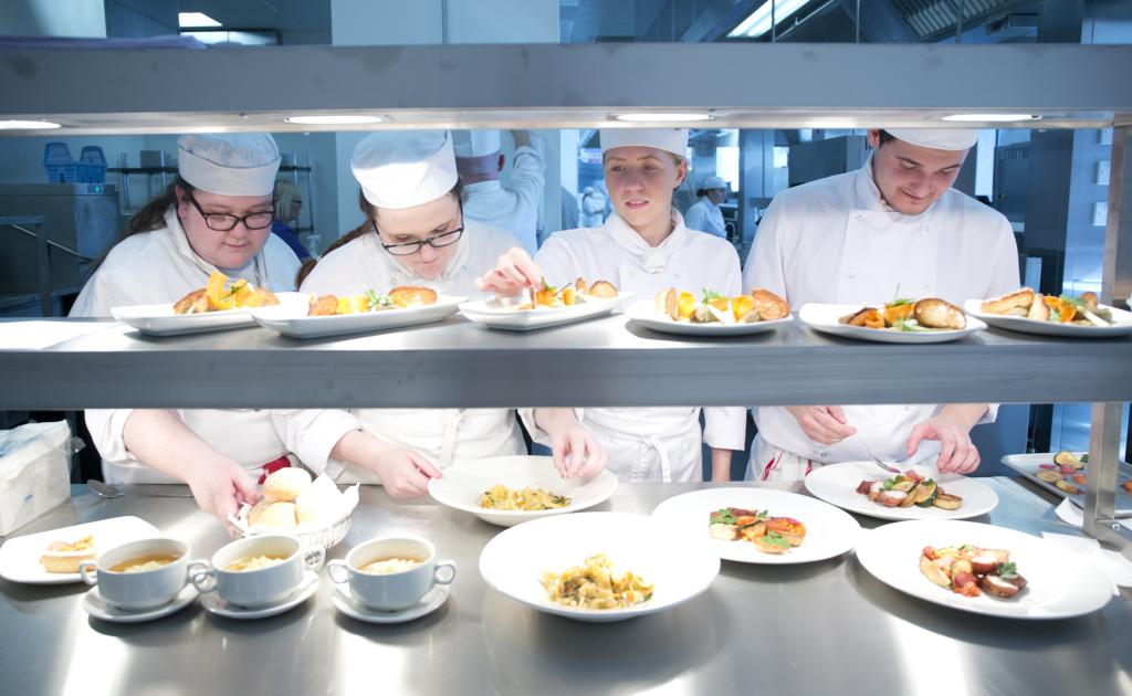 Culinary students standing in row behind counter preparing plates for serving.
