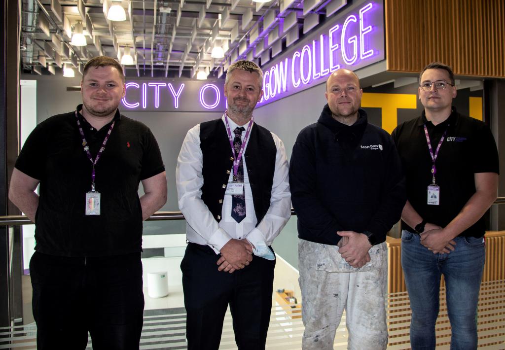 Charlie Kennedy, Andy McNicol, Jaemie Smith, Michael McEwan standing in a line with neon City of Glasgow College sign in background