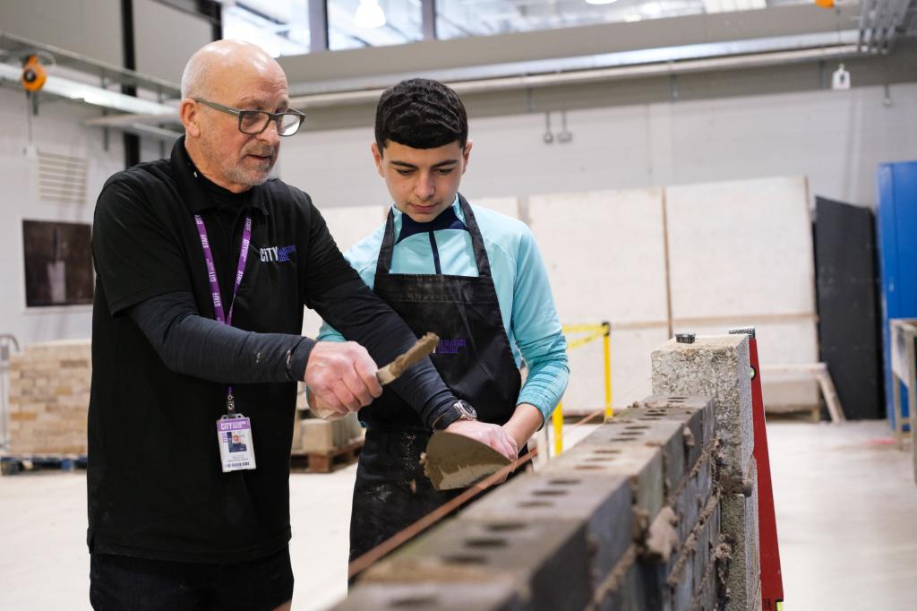 A lecturer demonstrating bricklaying to a pupil.