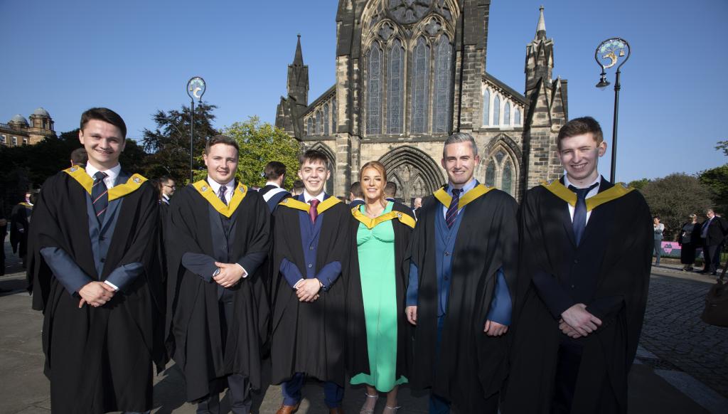 A group of students standing outside Glasgow Cathedral dressed in graduation gowns..