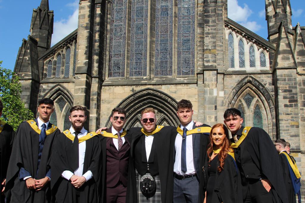 Six students lined up in graduation gowns outside Glasgow Cathedral