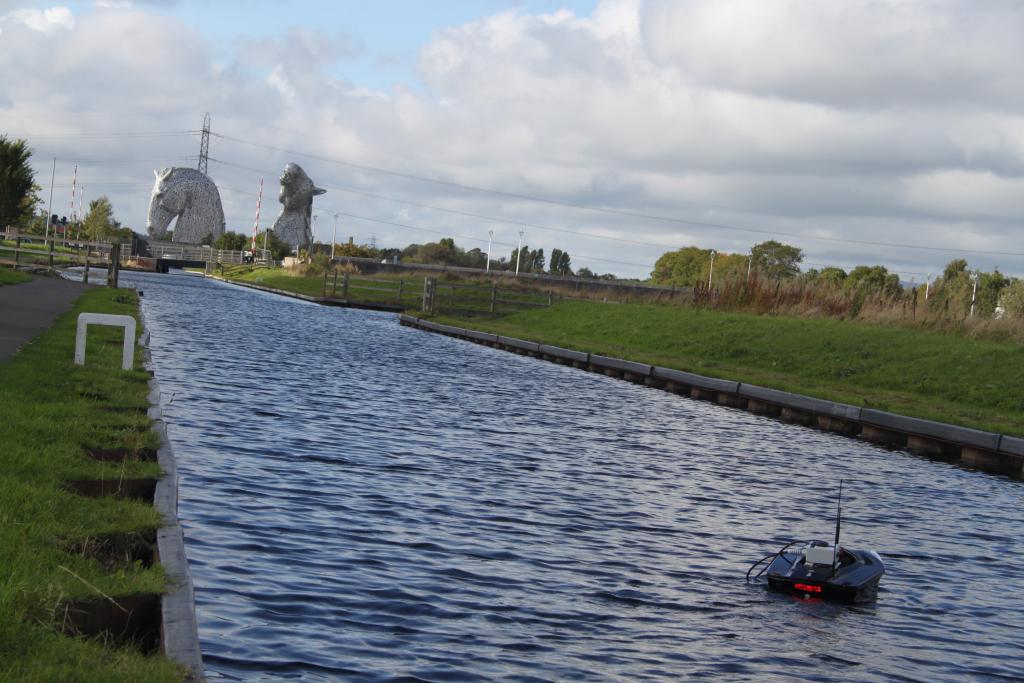 Aquabot, a water quality monitoring platform using digital sensor technology floating on a canal with the Kelpies in the bckground.