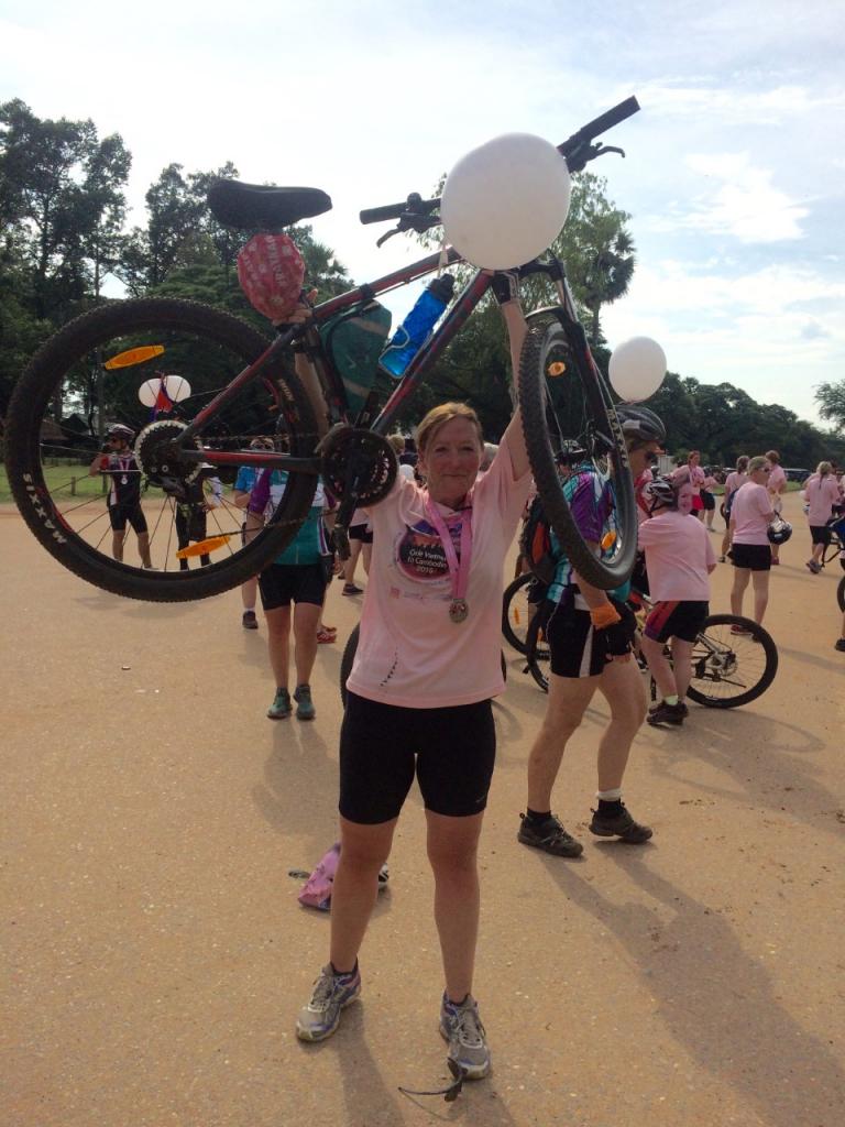 Kerry Bamber raising her bike above her head at finishing line of cycle challenge in Cambodia