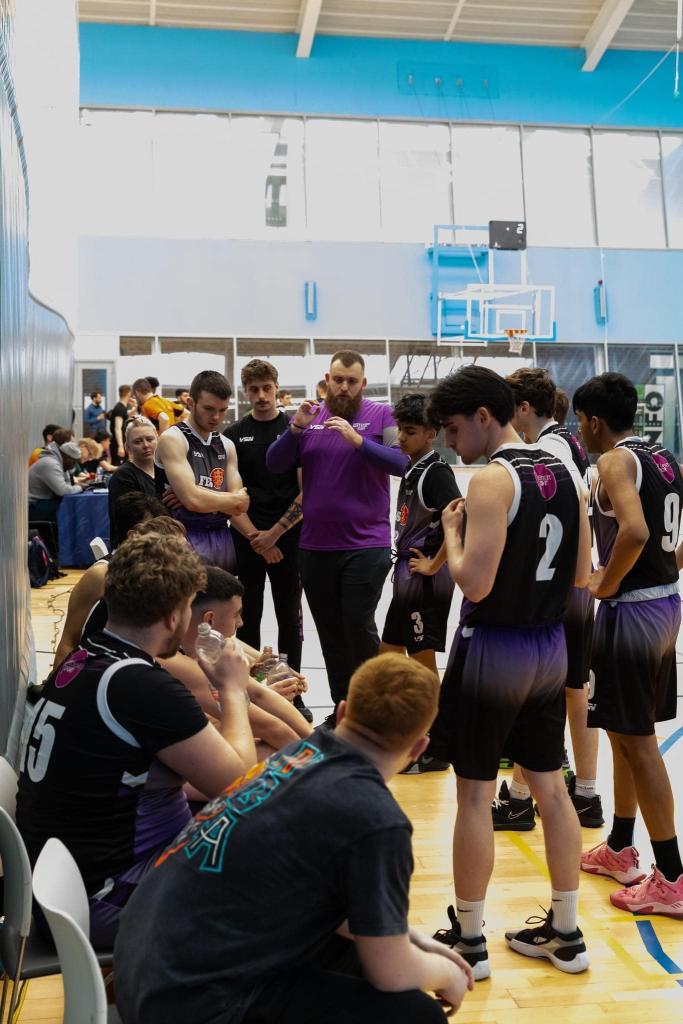 Mens basketball team in a group chatting with the coach.