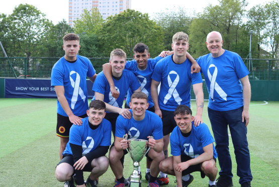 Eight students wearing football strips holding a cup 