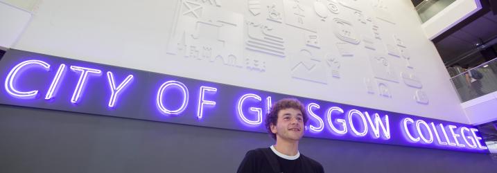 Student at an Open Day standing in front of a purple neon City of Glasgow College sign