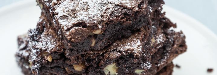 A light blue plate with two chocolate brownies stacked on it with a dusting of icing sugar on the top