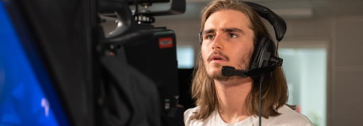A student wearing a headset working with a TV camera