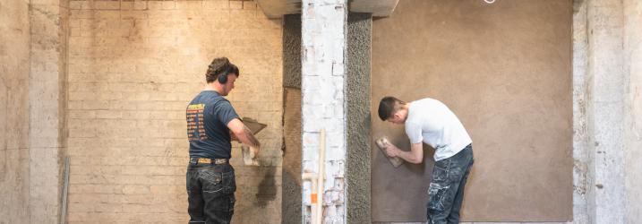 Two students in the construction workshop plastering a wall.