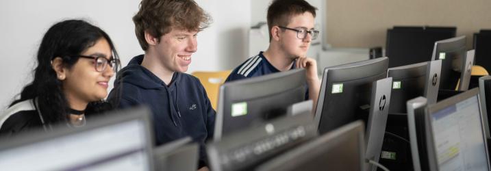 Three students sitting in a working on computers.