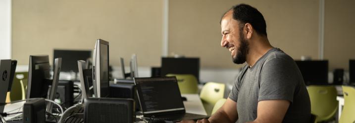 A student sitting at a desk in a classroom laughing looking at a computer screen