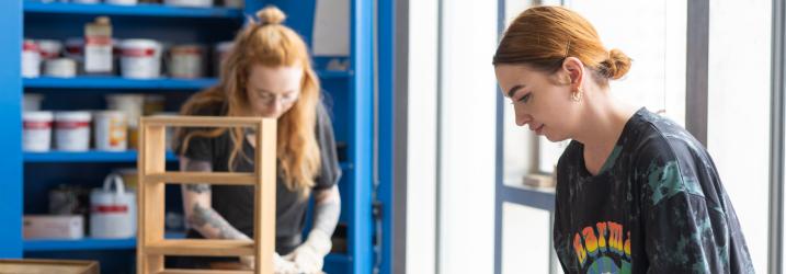 Two students in a workshop working on a piece of furniture