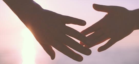 Two joined hands with the sunset in the background.