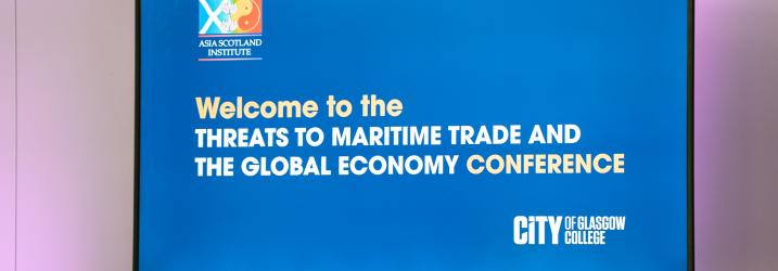 A TV screen with 'Welcome to the threats to Maritime Trade and the Global Economy Conference