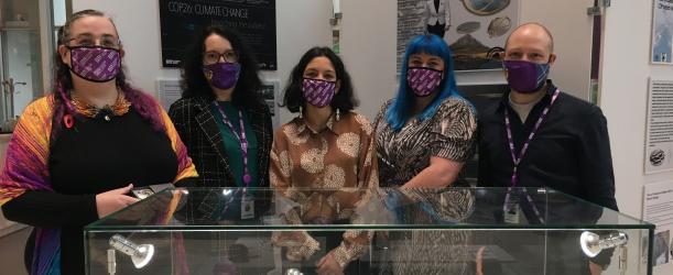 Four jewellery students standing behind a exhibition case with their work in it.