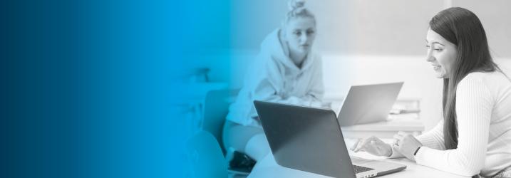 Blasck and white image of two students sitting at desk chatting and working on laptops with a blue overlay.