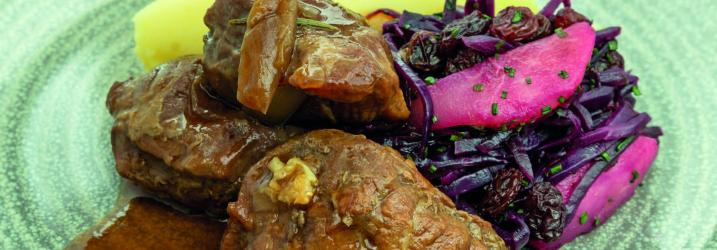 A green plate with cooked red meat and gravy on one side and red cabbage on the other.