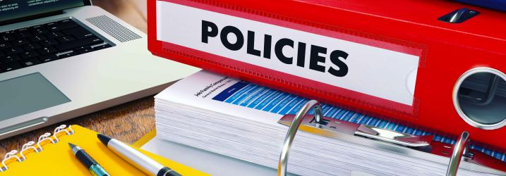 Policies folders, notebook and pen on a desk.