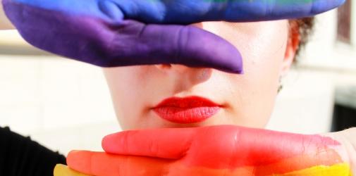 Close up of a face with rainbow painted hands in front of it.