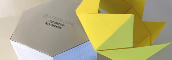 A grey paper hexagonal box with a yellow paper crown at the side.