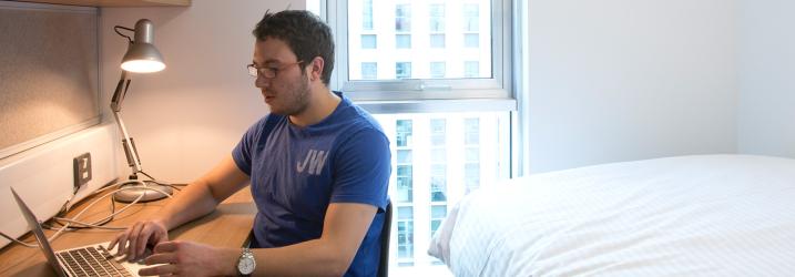 Student working at laptop in student accommodation room