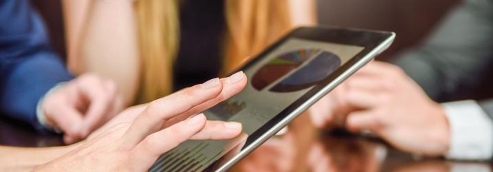 Hands holding a tablet with three people blurred in the background