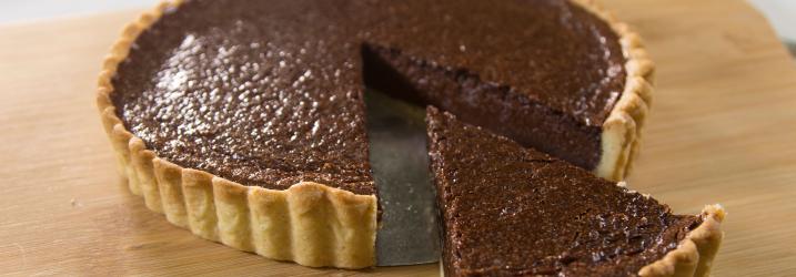Close up of a chocolate tart with a slice cut out sitting on a wooden board