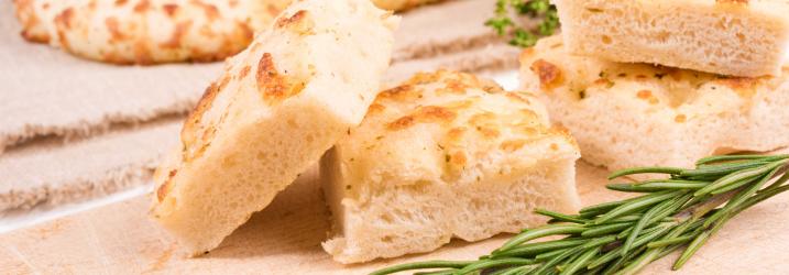 A wooden board with chunks of bread and a sprig of rosemary on it.